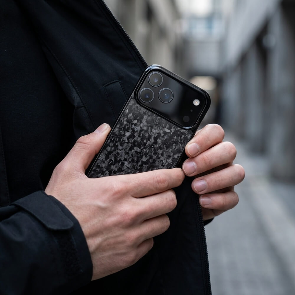 Photography, unknown artist, a person's hands retrieving a black iPhone with three prominent camera lenses and a dark grey mottled carbon fiber case from a black jacket in an urban alley